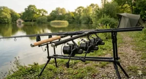A full three-rod setup of 12ft carp rods on a rod pod with bite alarms, bobbins, and a bivvy in the background at a British fishery.