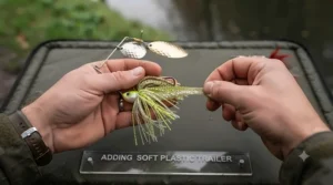 Close-up of adding a soft plastic shad or curly-tail grub to a spinnerbait to increase lure volume.