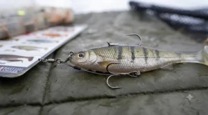 An extreme close-up shot focusing on the intricate details of a stinger rig attachment, showing a sharp treble hook connected by a wire trace to a large soft plastic shad lure.