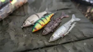 A photographic arrangement of four weedless-rigged soft plastic lures, meticulously rigged to navigate through heavy winter cover, resting on a damp, textured angling mat.