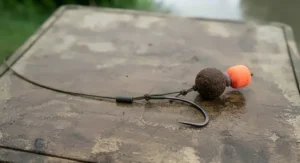 Detailed view of a large barbed hook and hair-rigged pellet bait designed for bottom-feeding river catfish.