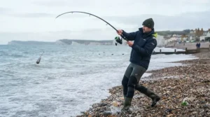 Angler demonstrating sea fishing casting techniques with a powerful beachcaster rod from the shore.